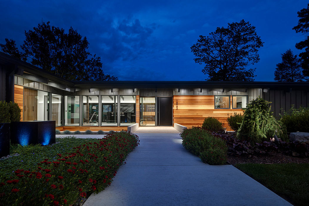 Modern exterior with glass walls, wood paneling, landscaped walkway, and evening lighting.