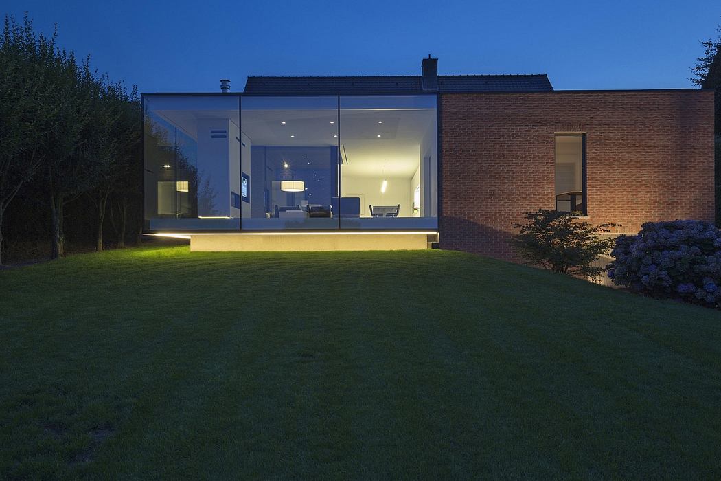 A contemporary, glass-walled home with a spacious yard and illuminated interior features.
