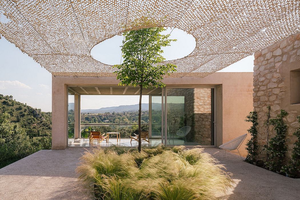 Expansive glass walls open to a lush terrace shaded by a canopy of greenery.