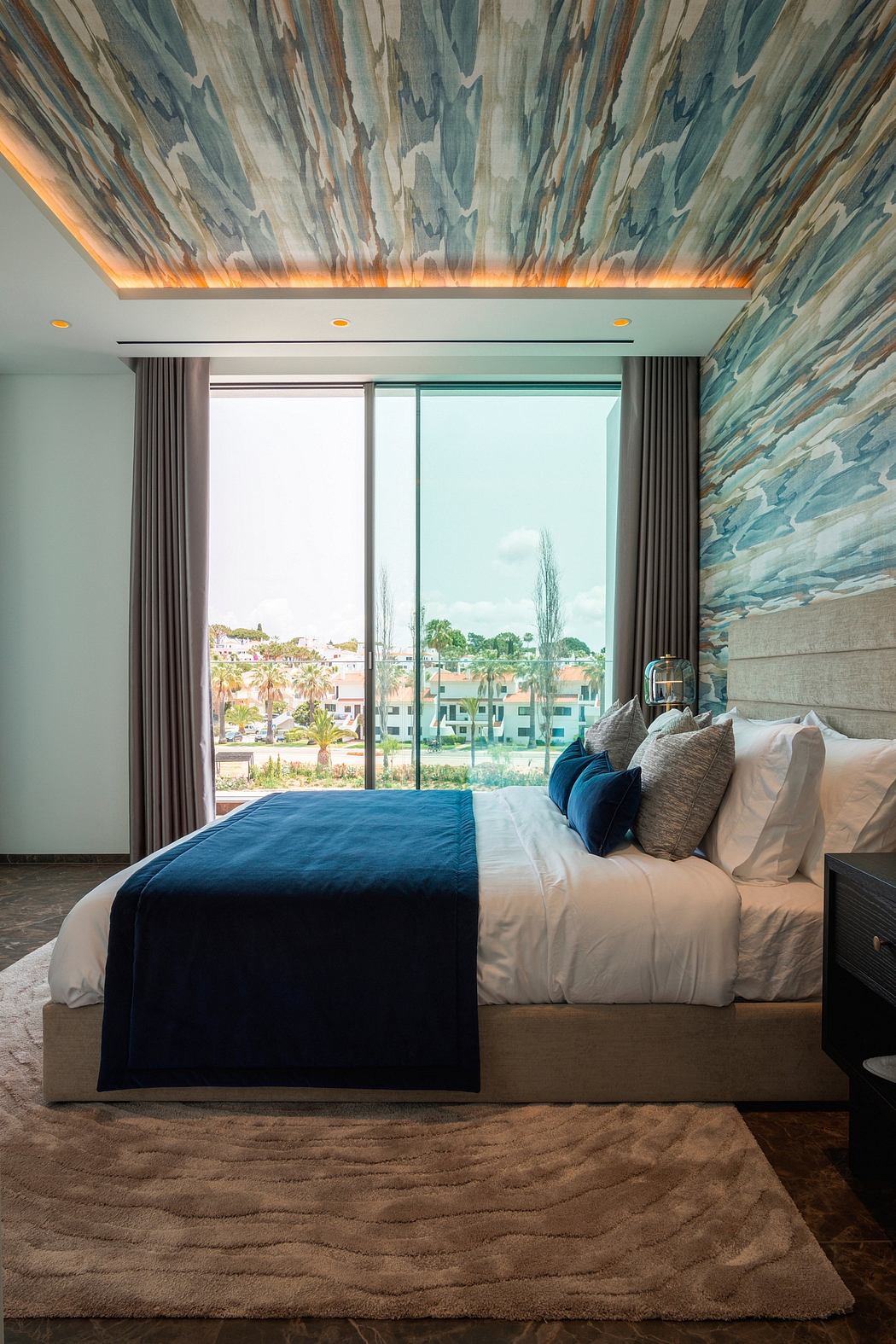 Spacious bedroom with abstract wall patterns, large windows, and plush furnishings.