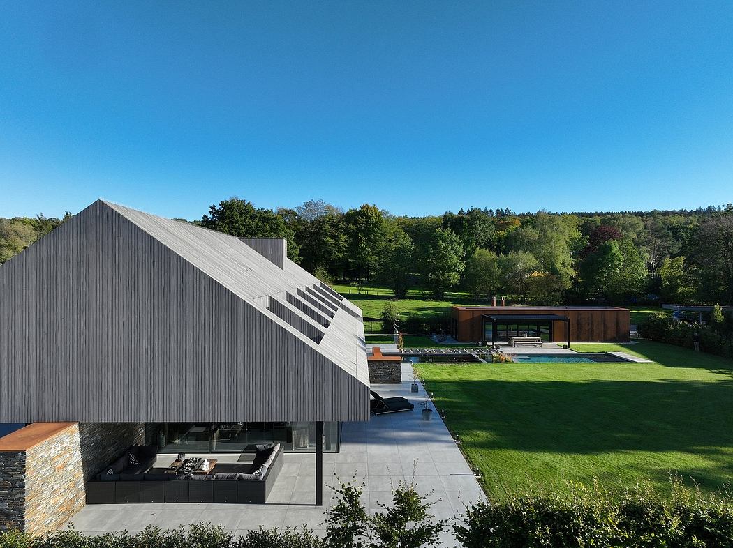 A modern, angular home with a large outdoor patio and expansive green lawn nestled in a forested landscape.