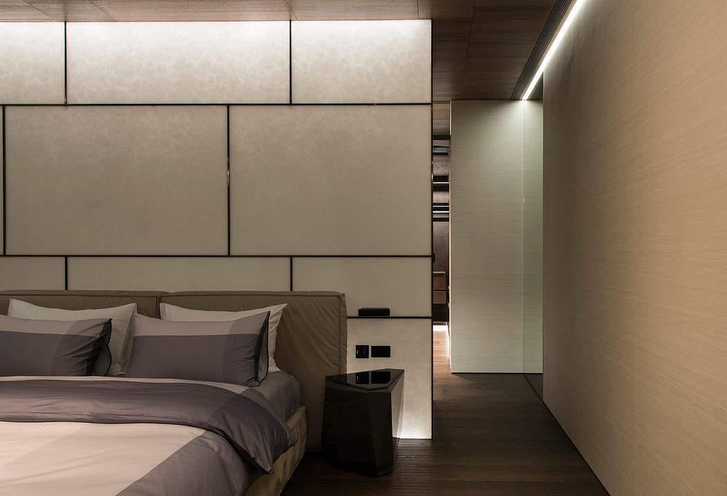 A modern, minimalist bedroom with a light-colored wall, recessed lighting, and a sleek, built-in shelving unit.
