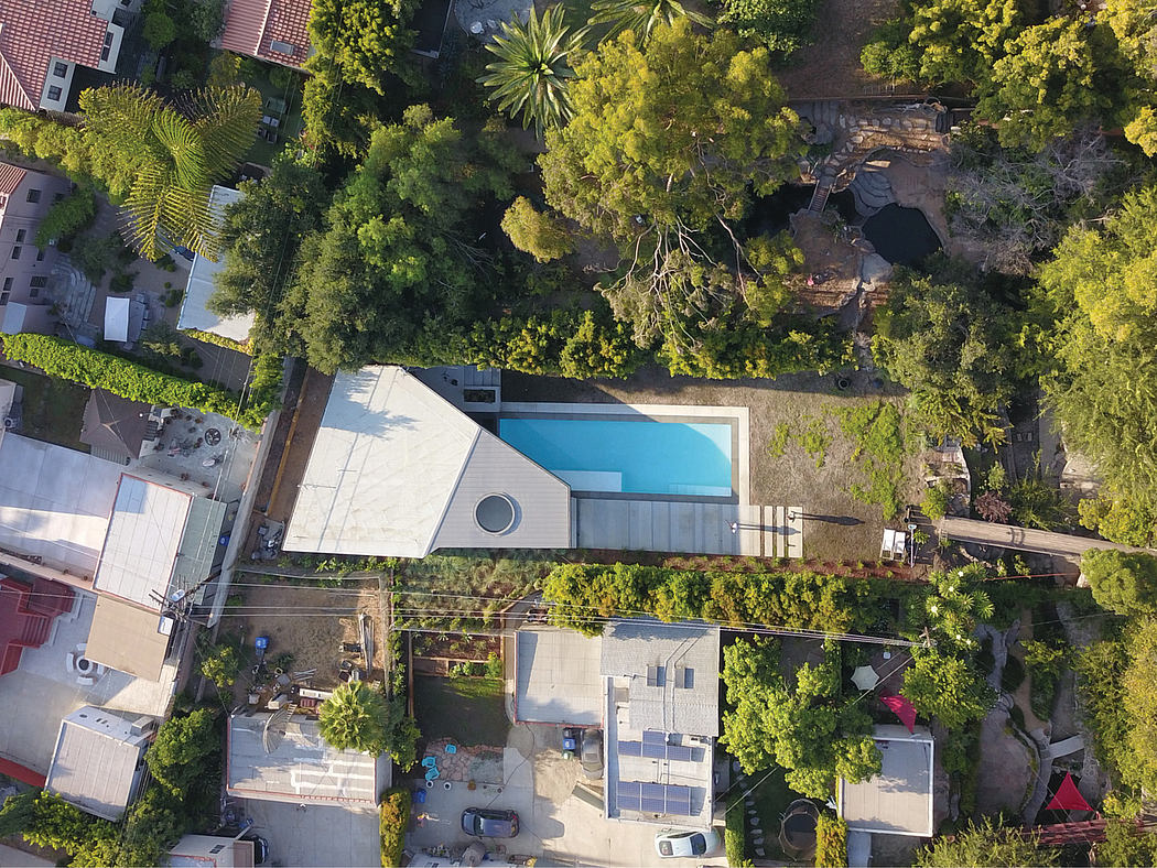 Aerial view of a modern home with a swimming pool surrounded by lush vegetation.