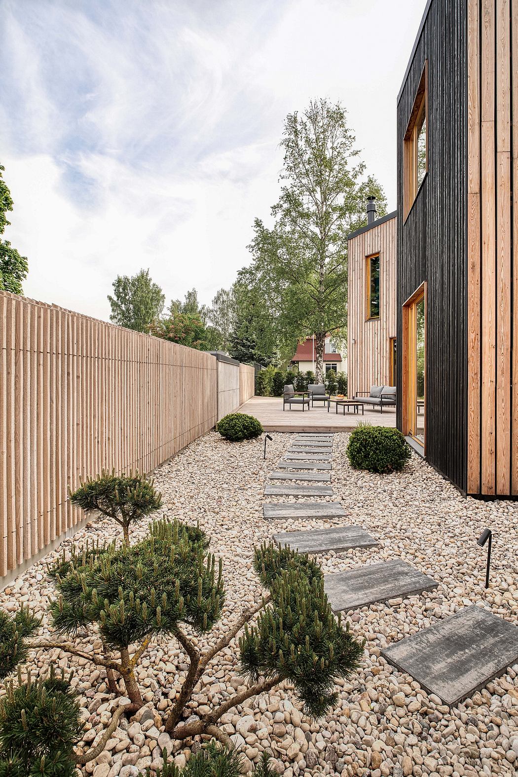 Sleek modern architecture with wooden siding and gravel paths leading to patio area.