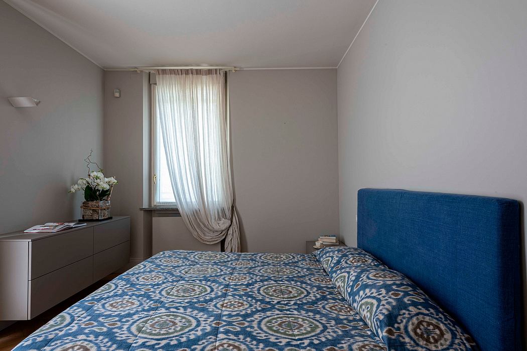 Minimalist bedroom with blue patterned bedding, gray curtains, and modern furniture.