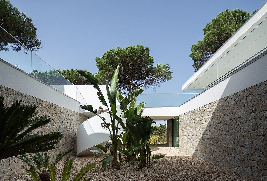 A modern, open-concept outdoor courtyard with stone walls, glass panels, and lush tropical plants.
