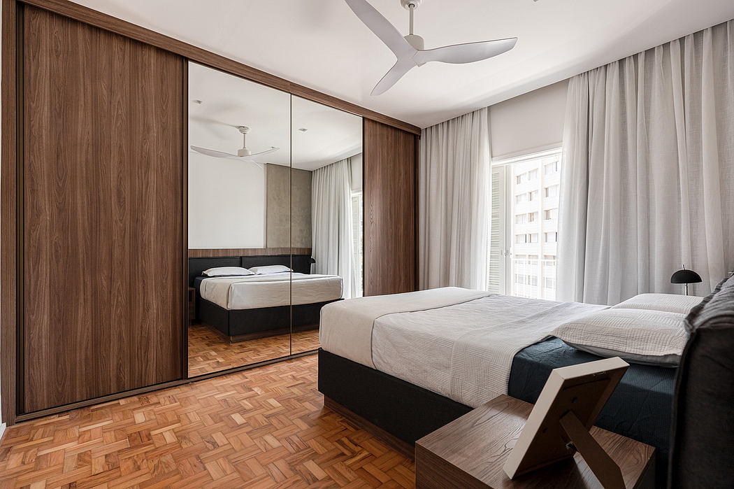 Minimalist bedroom with wooden wardrobe, herringbone flooring, and large windows.