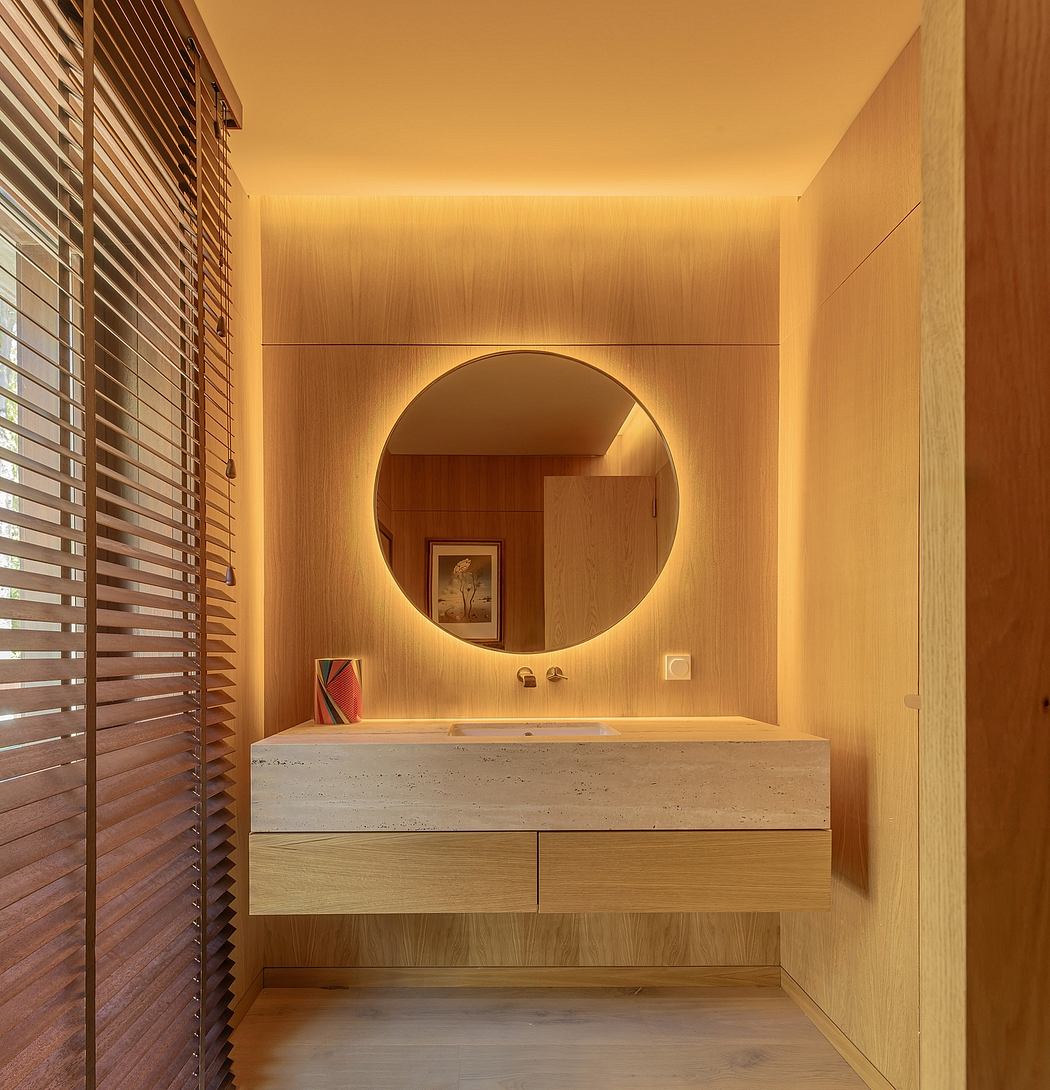 Modern vanity with circular mirror, stone countertop, and warm wood tones in bathroom.