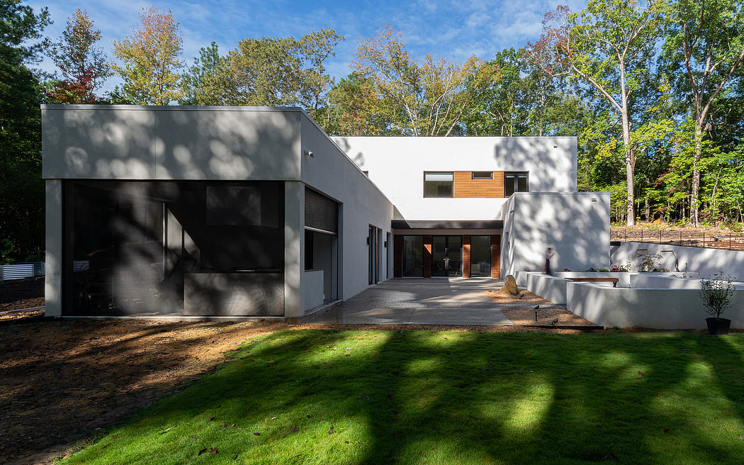 Modern, minimalist home featuring a sleek, gray exterior with a mix of glass and wood accents. Landscaped front yard with a lush, green lawn.