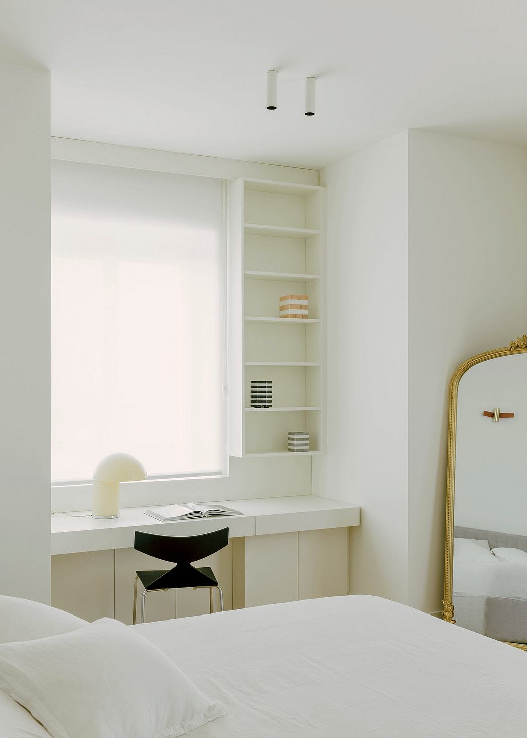 A bright, minimalist bedroom with built-in shelves, a desk, and a gilded mirror.