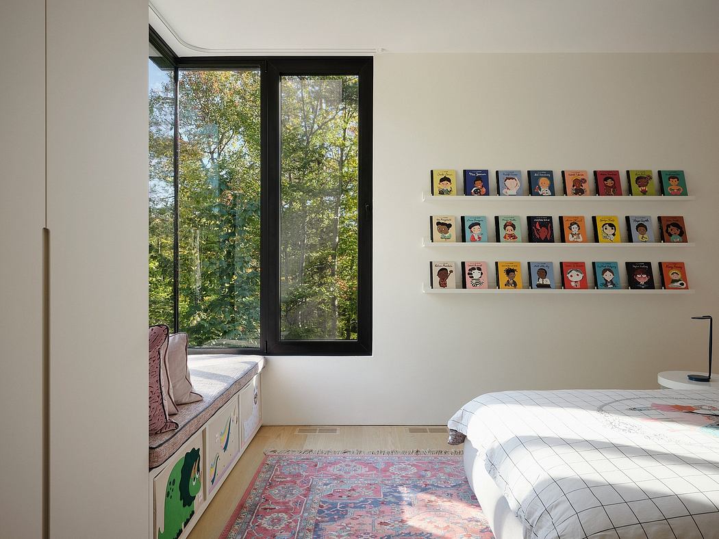 A cozy bedroom with floor-to-ceiling windows overlooking a lush forest, and a vibrant array of book covers displayed on the wall.
