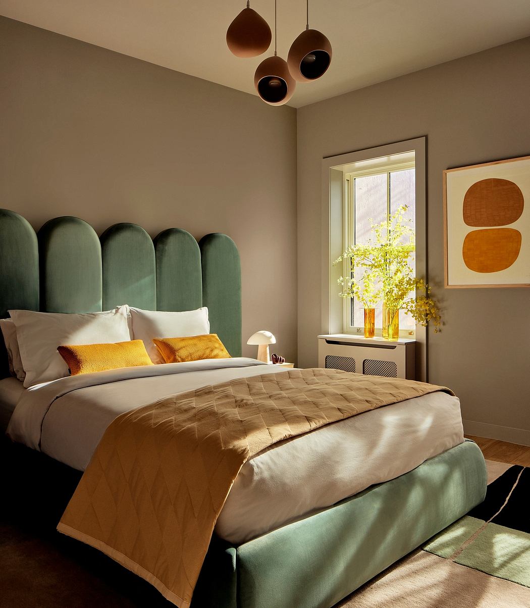 Cozy bedroom with plush velvet headboard, suspended lighting, and artwork.