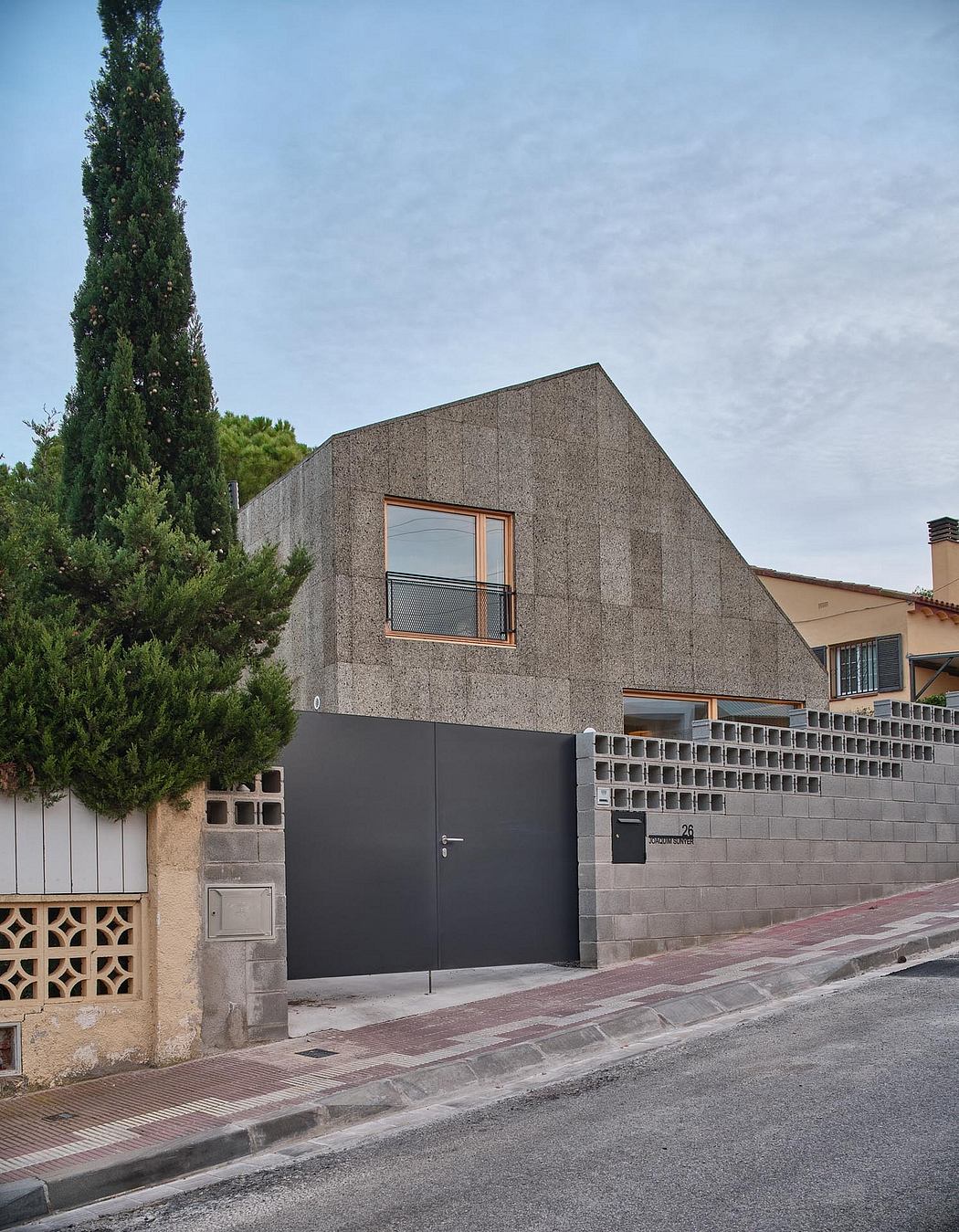 Modern two-story building with textured concrete facade, wooden window frames, and gate.