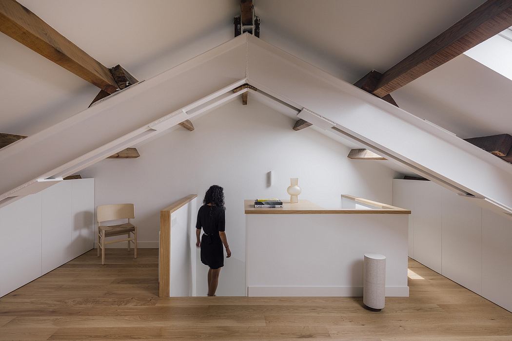 An airy, minimalist attic space with wooden beams, shelving, and a person in a black dress.