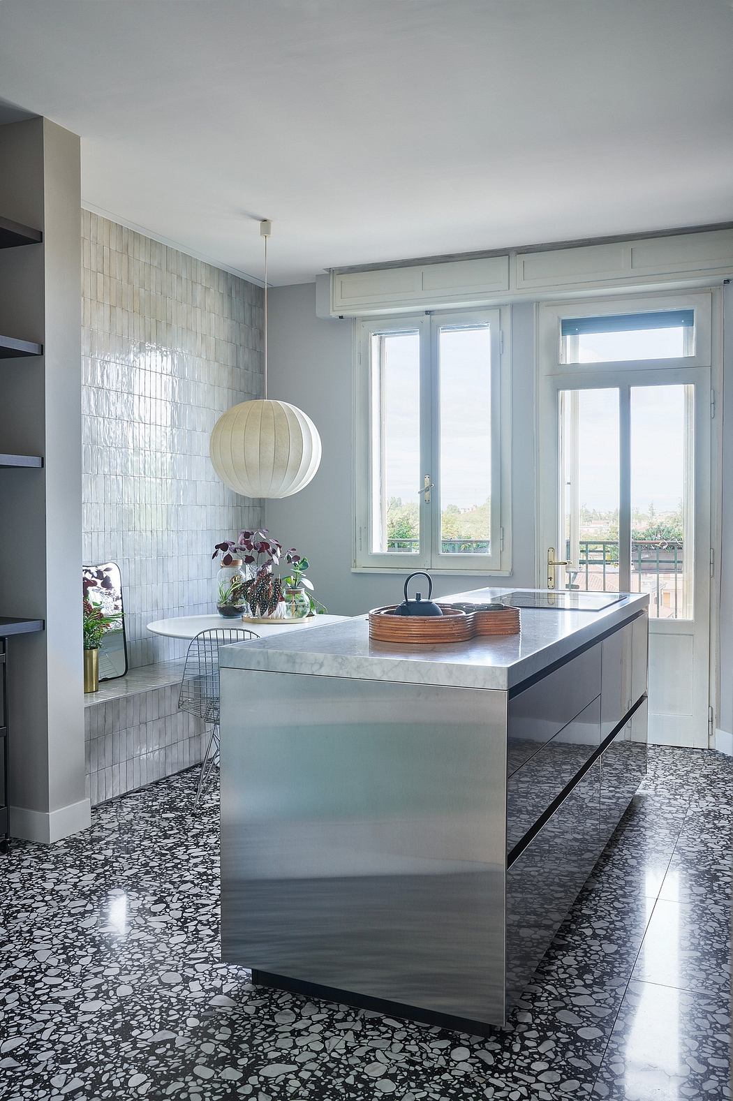 A sleek, modern kitchen with stainless steel countertops, tiled walls, and a white pendant light.