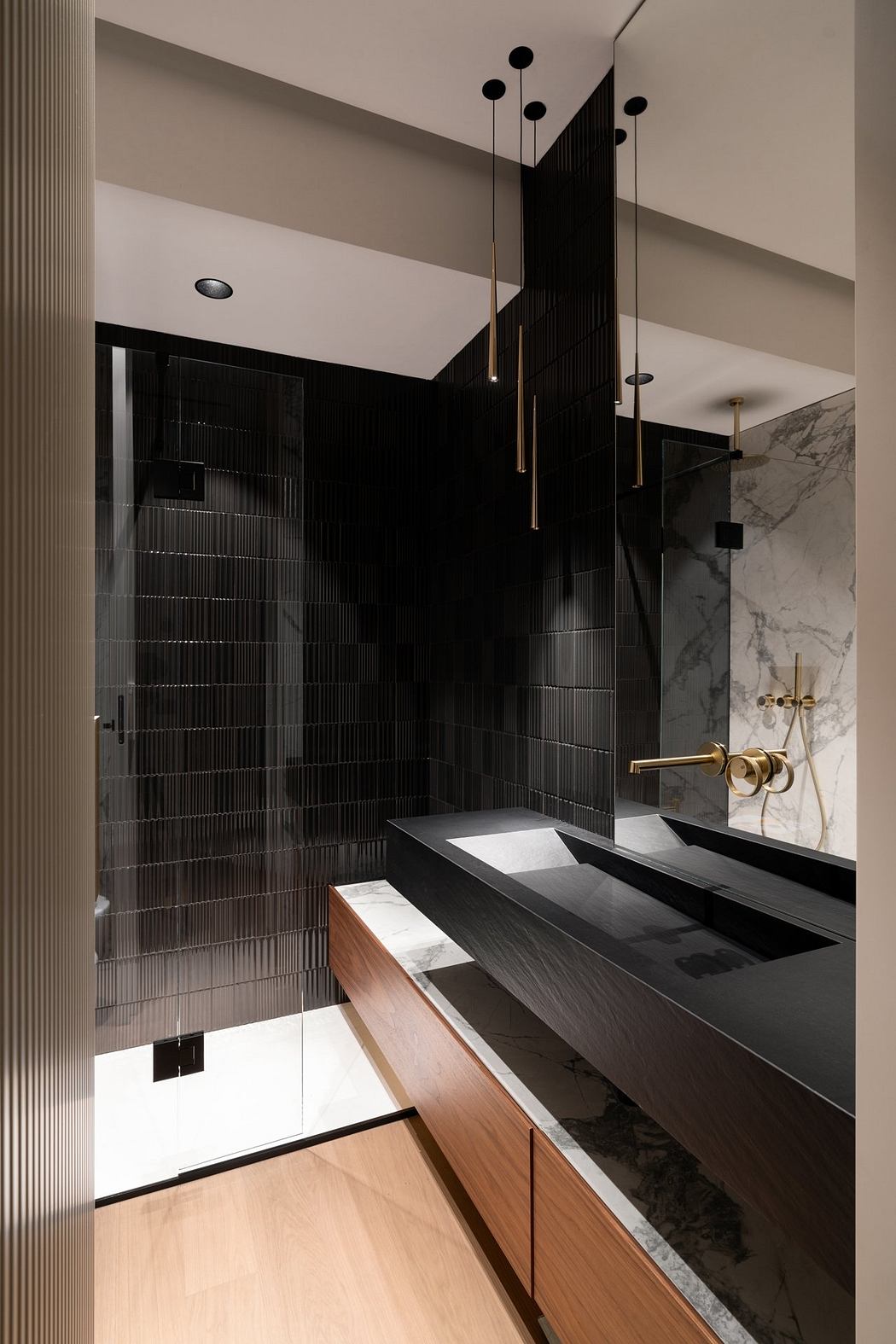 Sleek black tiled walls, brass fixtures, and a marble vanity create a modern, luxurious bathroom.
