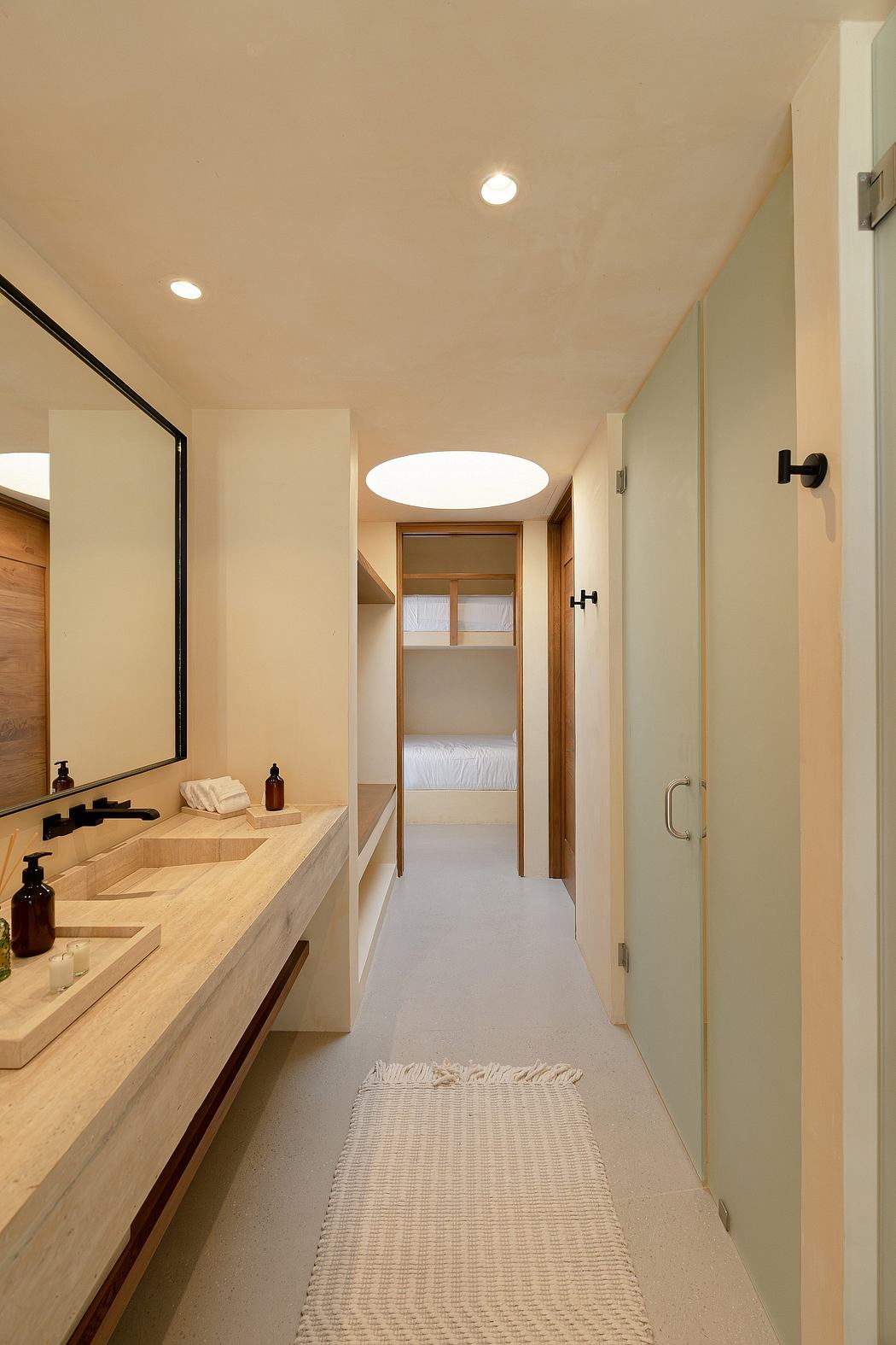 A modern, minimalist bathroom with a wooden vanity, recessed lighting, and a glass door.