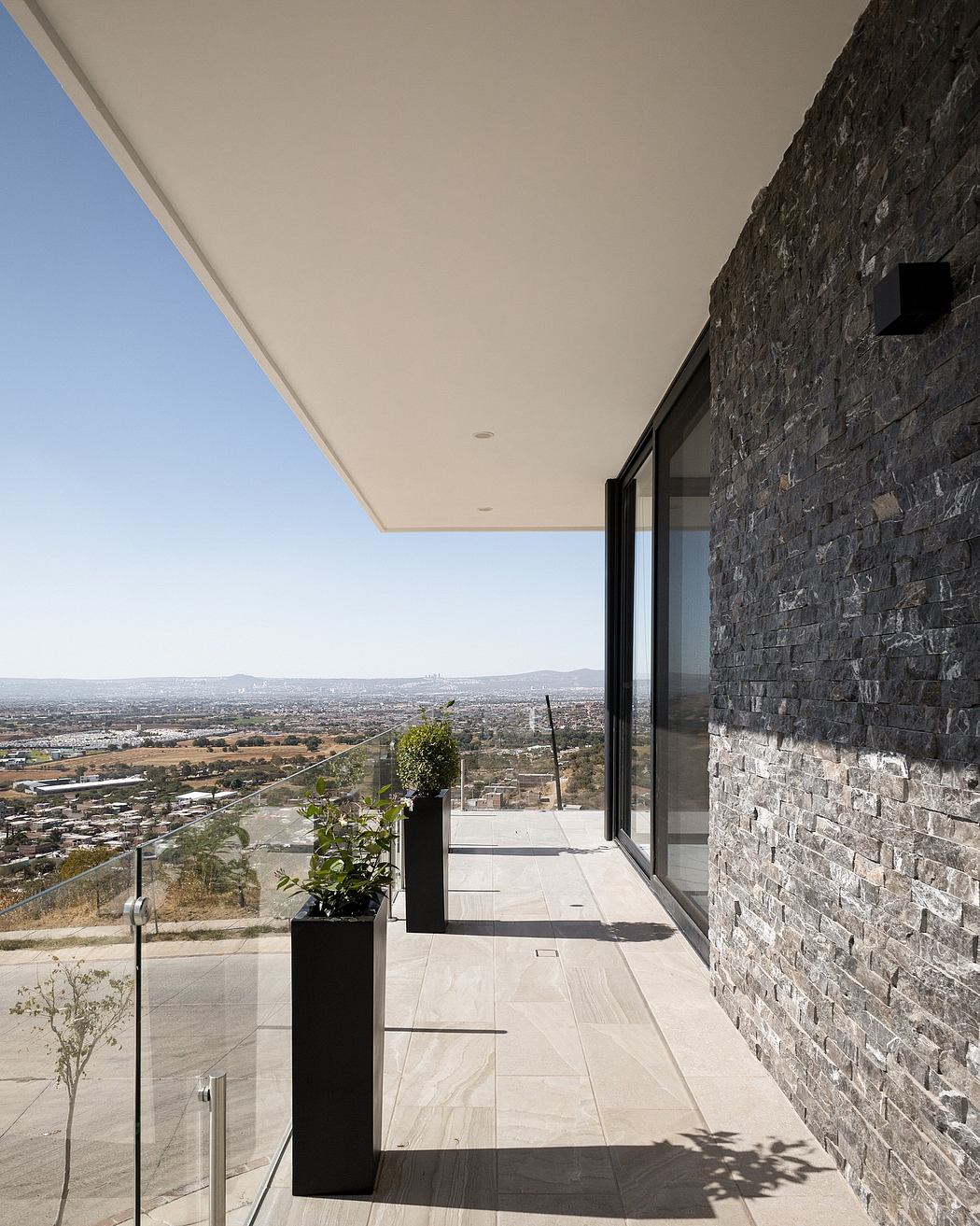 Expansive stone wall, sleek glass panels, and a sweeping cityscape vista beyond.