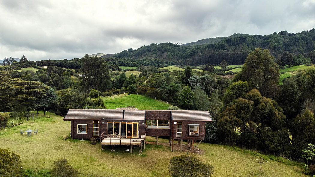 A rustic wooden cabin nestled in a lush, hilly landscape with a wraparound deck.