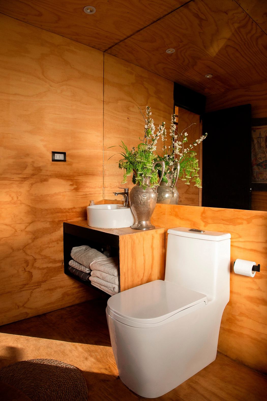 A cozy wooden bathroom with a floral arrangement, storage, and a modern toilet.