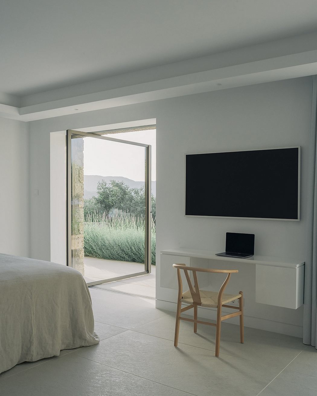 A minimalist bedroom with a large window offering scenic views, a black TV, and a simple wooden chair.