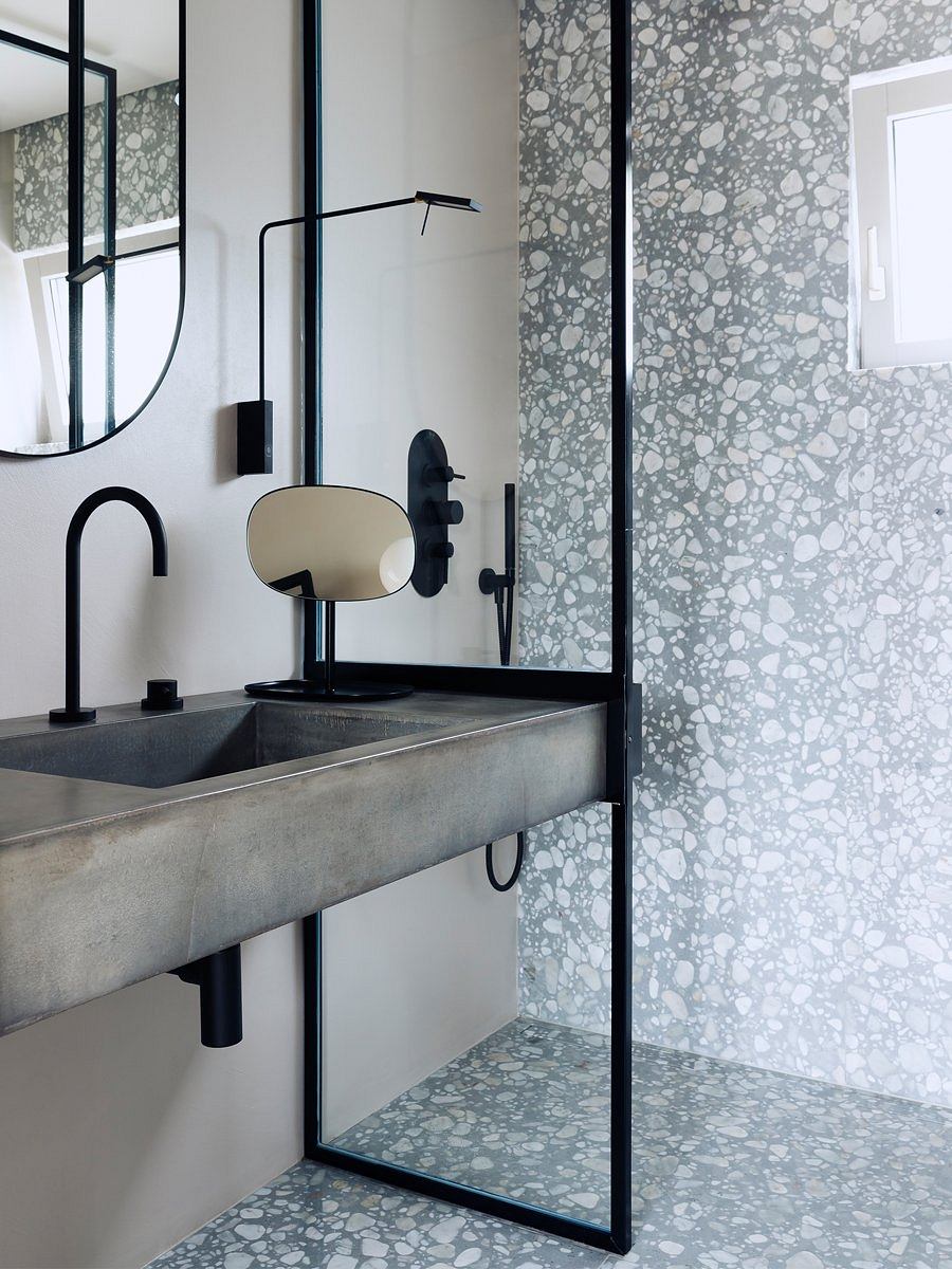 A modern bathroom with a concrete sink, black fixtures, and patterned tile walls.