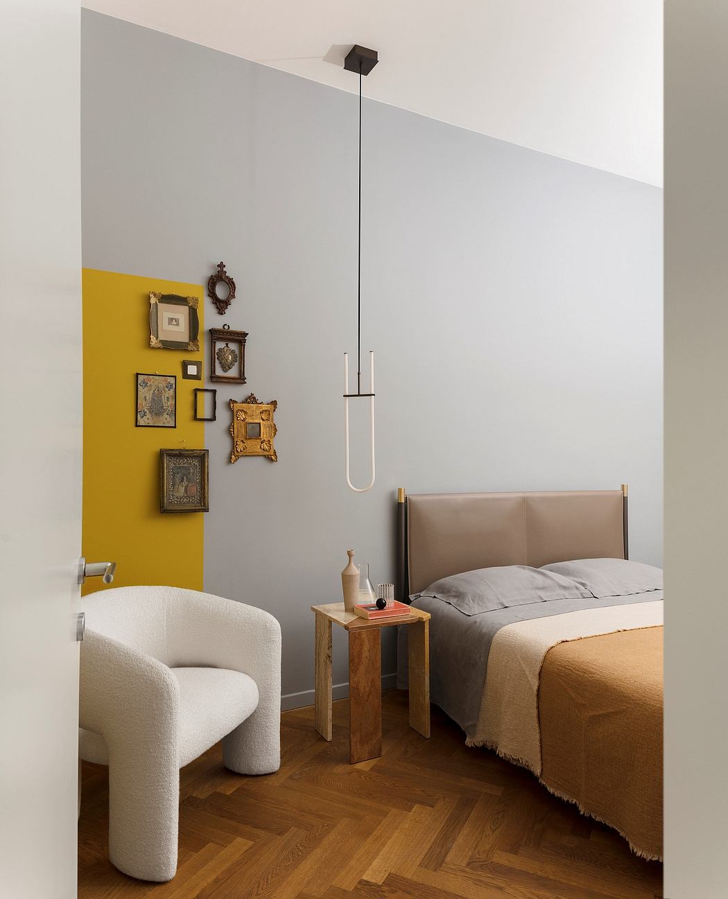 Cozy bedroom with warm wood floors, modern pendant light, and eclectic art gallery wall.