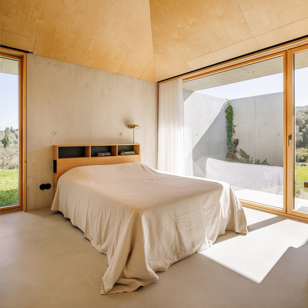 Minimalist bedroom with concrete walls, wooden ceiling, and large window overlooking nature.