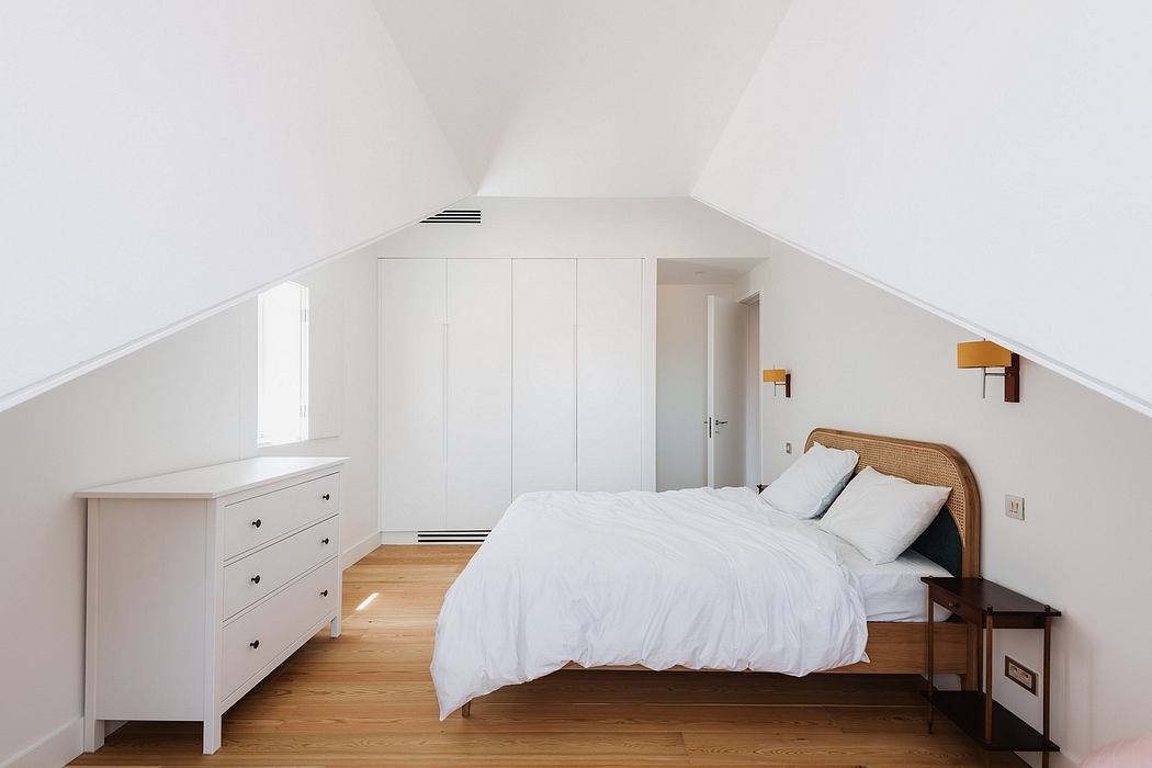 Bright, airy attic bedroom with sleek white built-in wardrobes and wood floors.