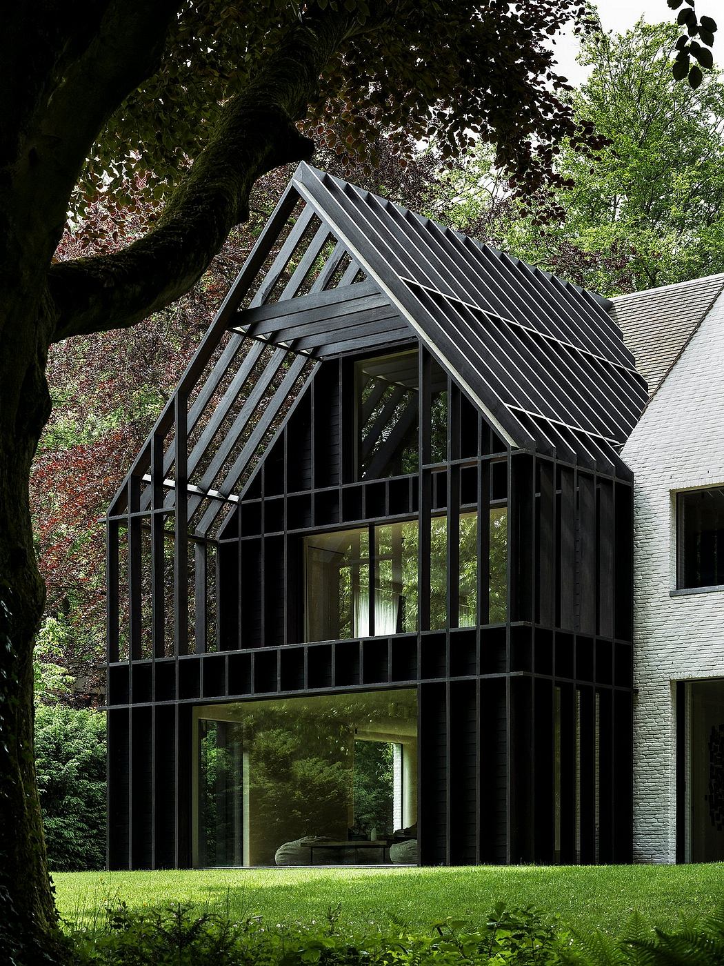 A modern, angular glass house nestled in a lush, forested setting. Striking architectural design.