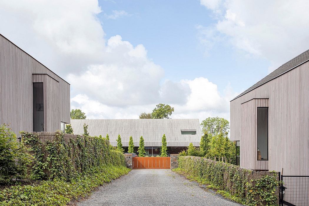 Modern gray buildings with gabled roofs, surrounded by lush greenery and gravel path.