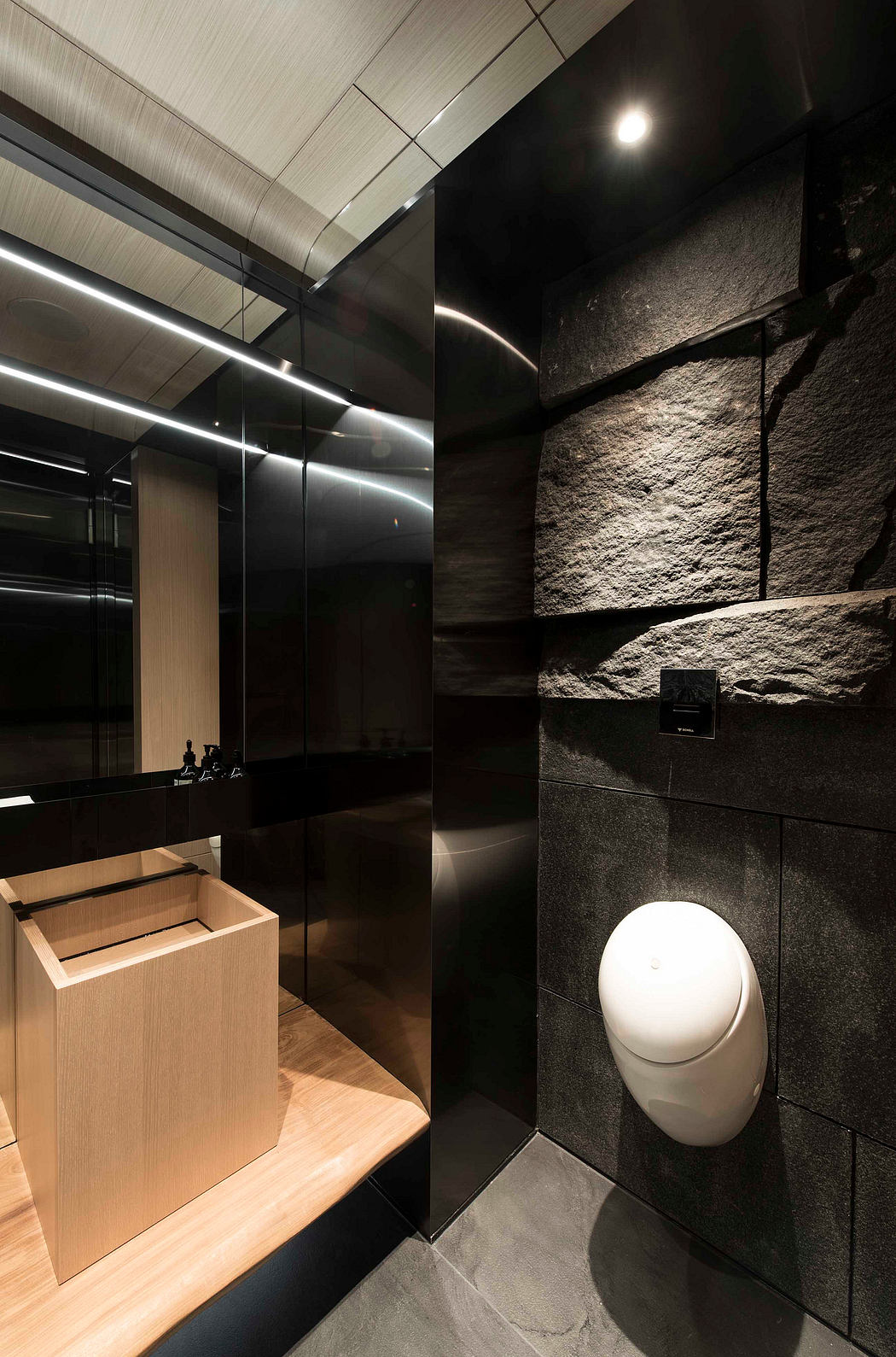 Sleek, modern bathroom design with wooden vanity, dark stone walls, and recessed lighting.
