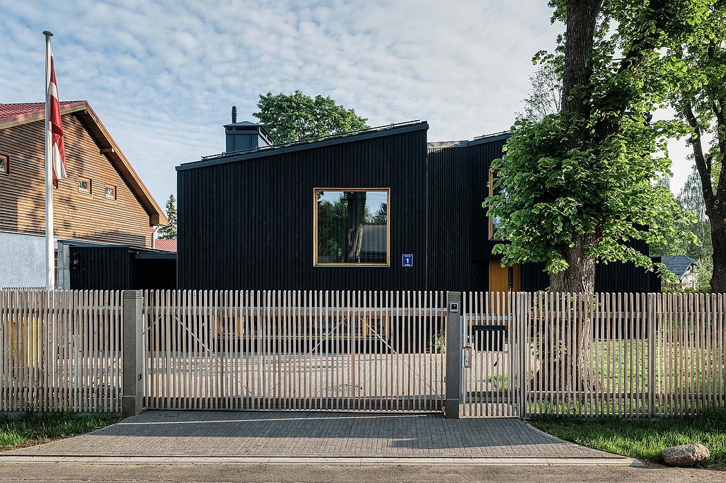 A modern, black-clad house with a prominent window, surrounded by a slatted wooden fence.