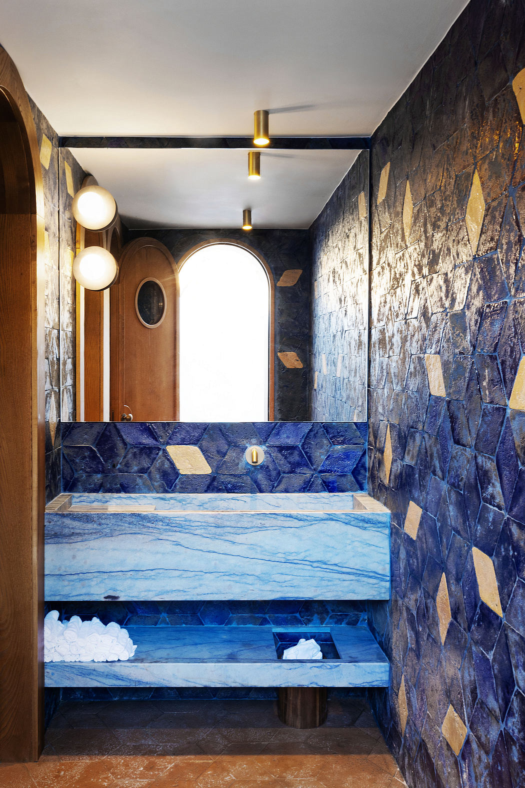 Striking bathroom design with bold blue stone tiles, arched mirrors, and elegant lighting.
