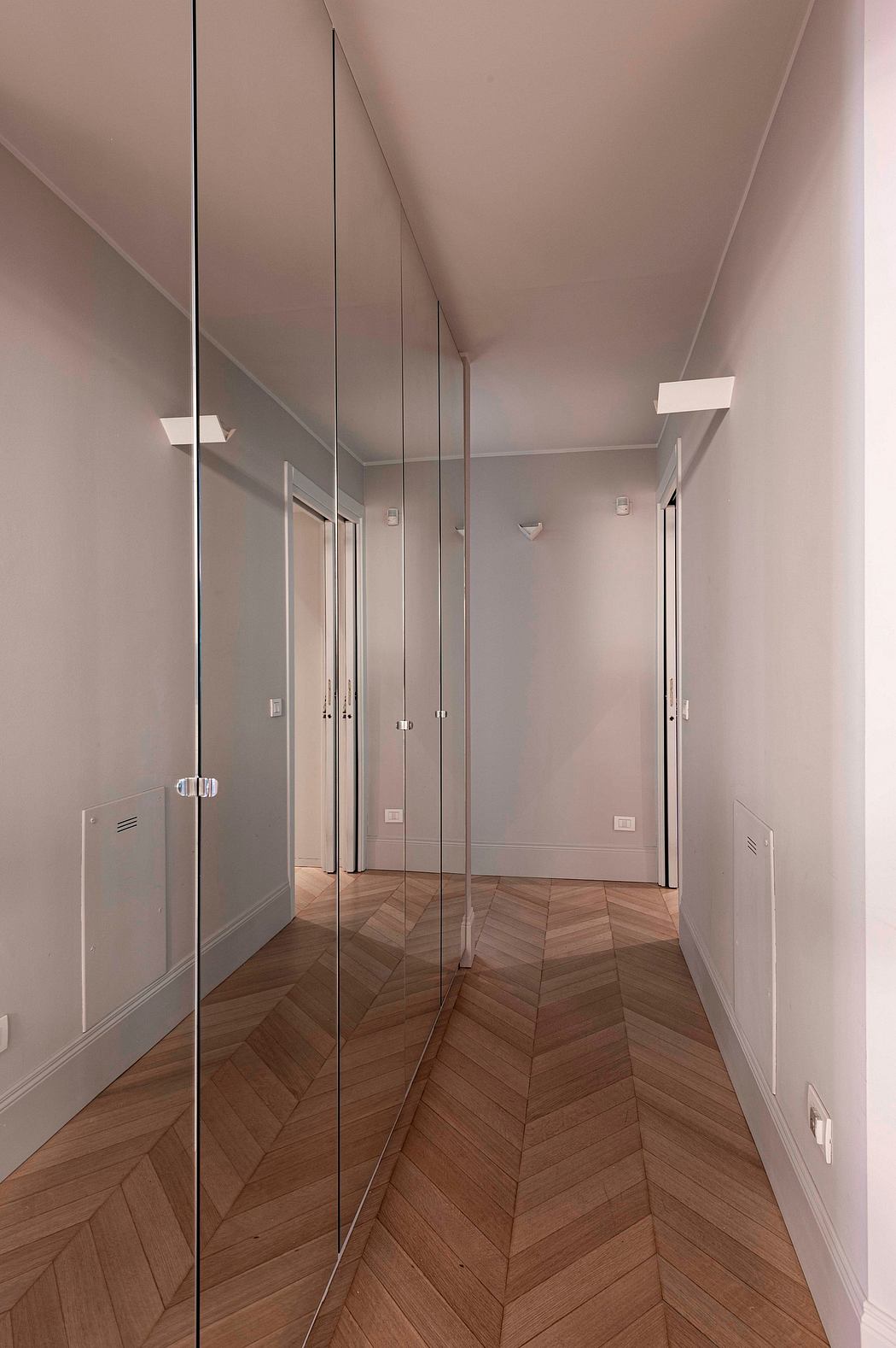 Elegant hallway with minimalist design, patterned wood flooring, and mirrored closet doors.