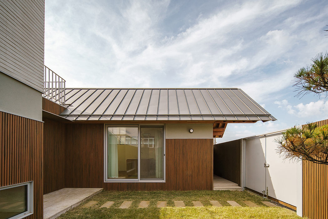 Modern metal-roofed home with wooden siding, glass doors, and a small grassy yard.