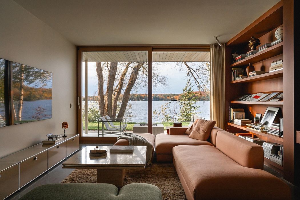 Cozy lakeside living room with floor-to-ceiling windows, wood-paneled walls, and a built-in bookshelf.