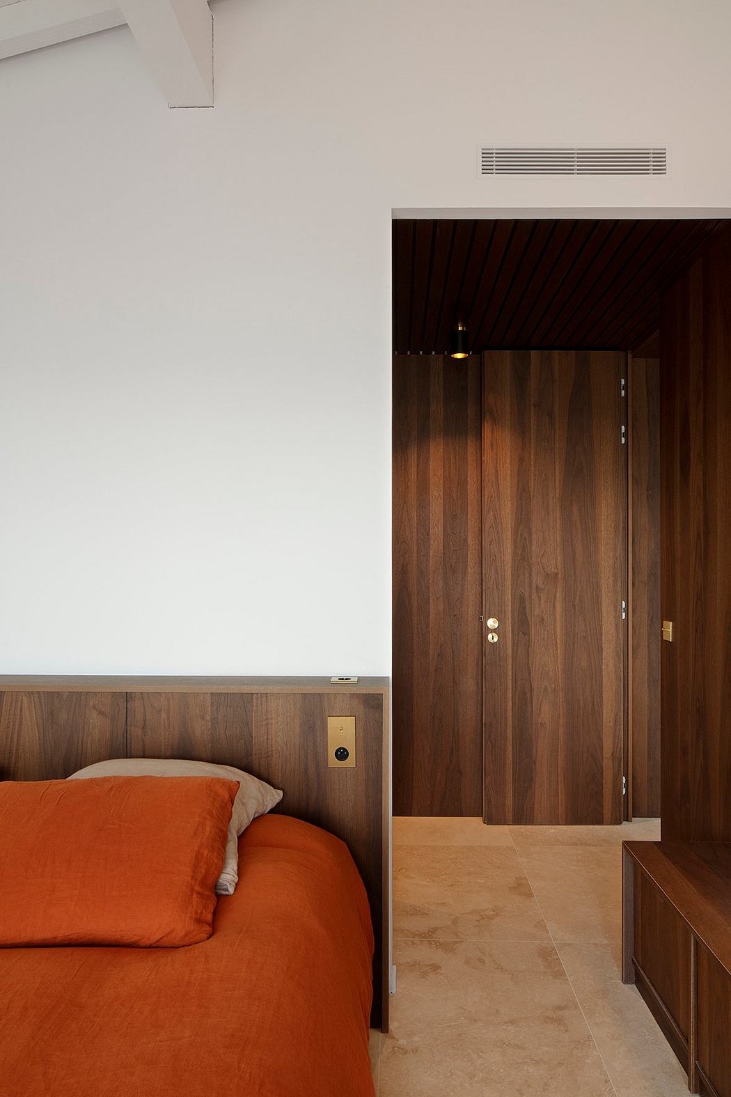Minimalist bedroom with warm wood accents, recessed lighting, and a striking orange sofa.