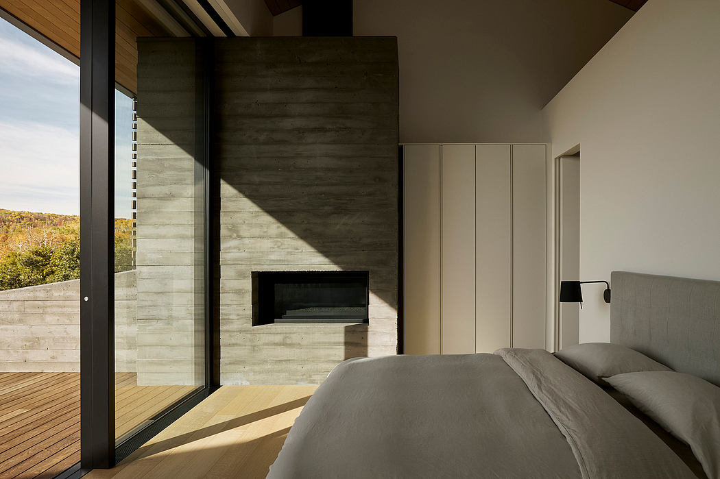 A modern bedroom with concrete walls, fireplace, and large windows offering scenic views.