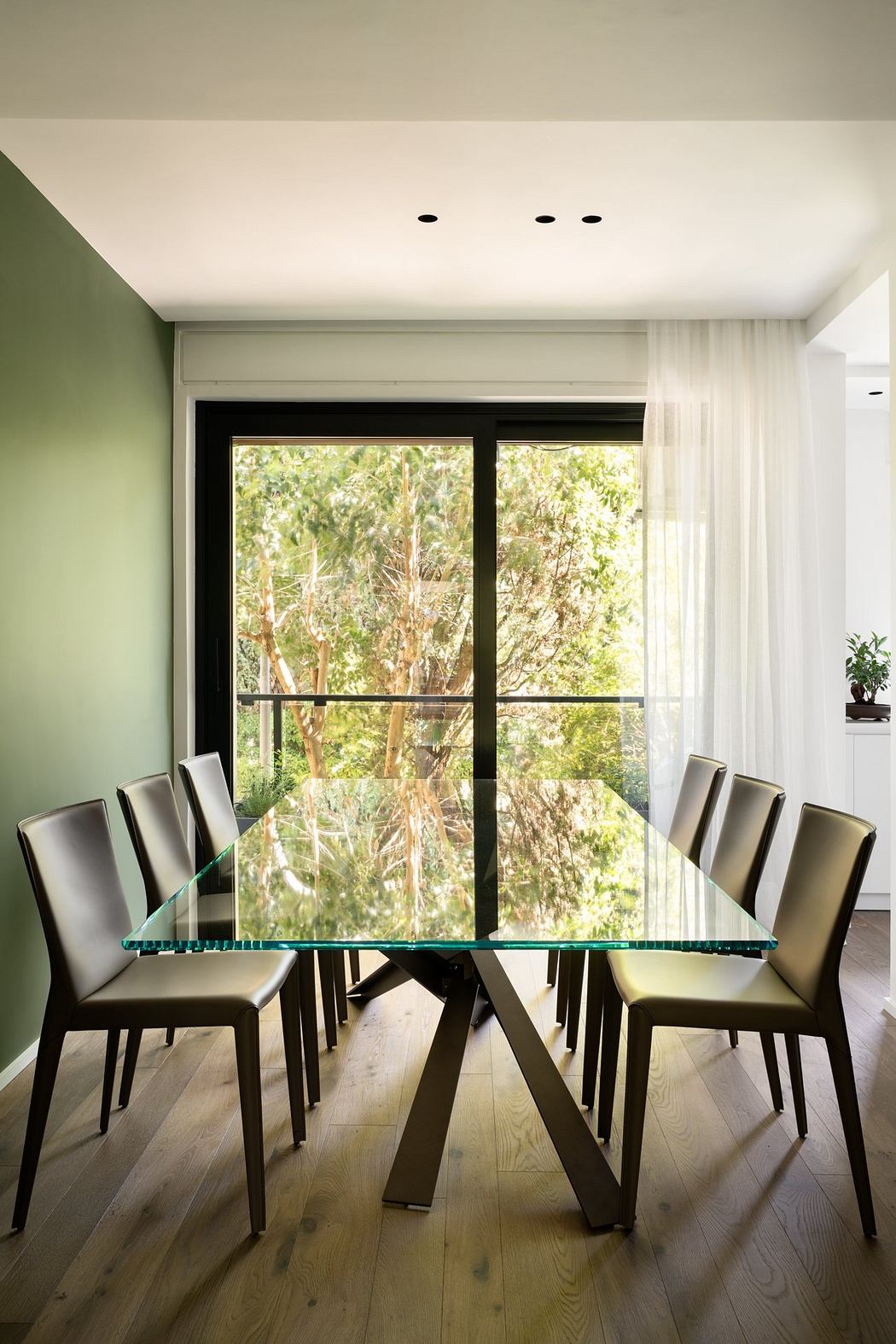 Striking modern dining room with glass table, leather chairs, and lush outdoor view.