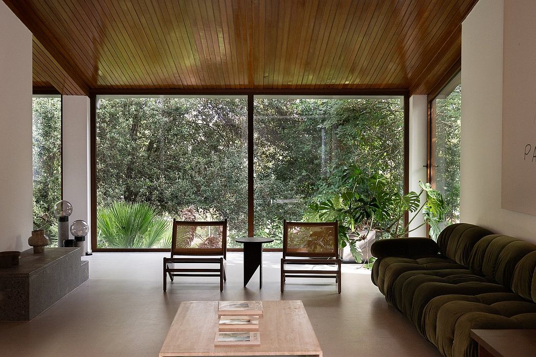 A cozy, modern living room with wooden ceiling, large windows, and lush greenery outside.