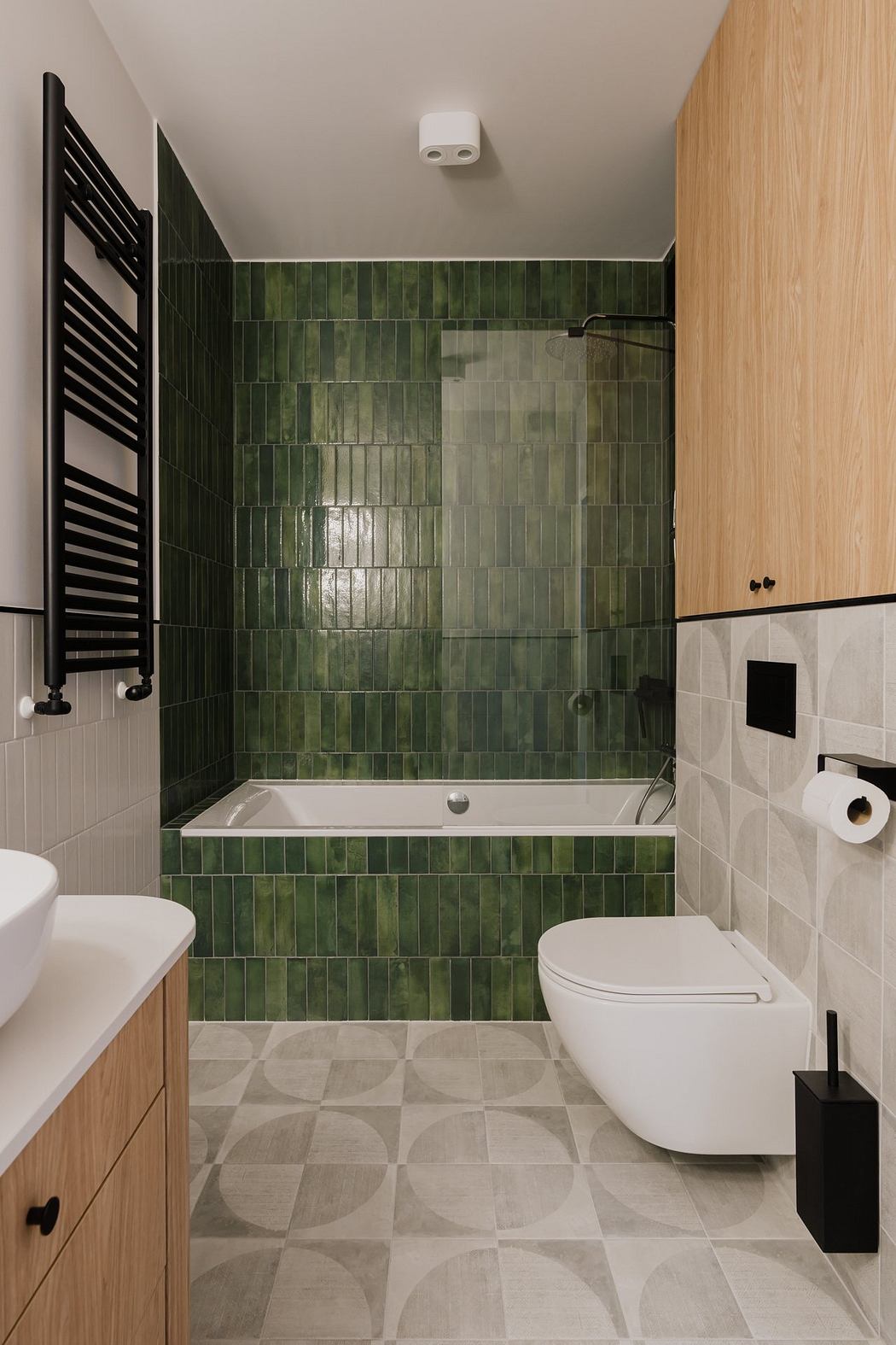 A modern bathroom with green ceramic tiles, a bathtub, and a toilet. The floor features a patterned tile design.