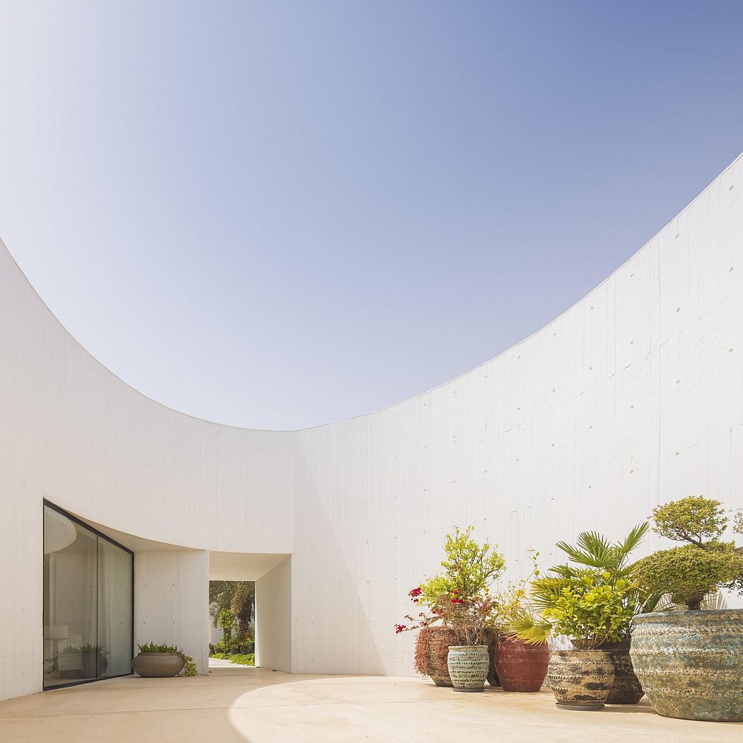 A modern, curved, white structure with large glass panels and lush tropical plants.