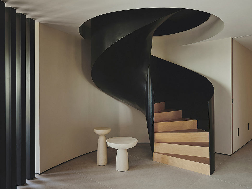 A curving black spiral staircase and minimal white furnishings in a modern interior.