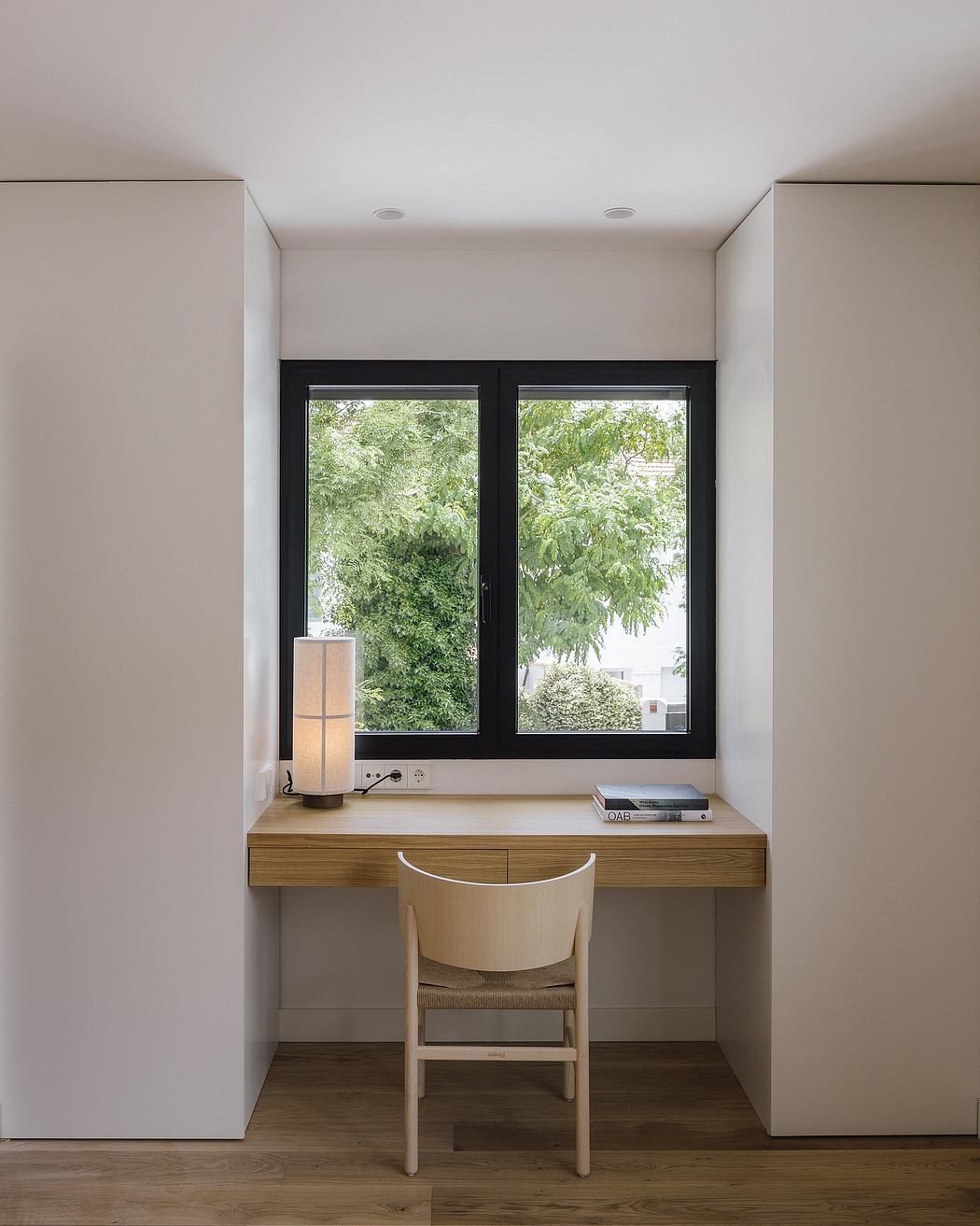 Minimalist home office with wood desk, black window frames, and nature-filled view.