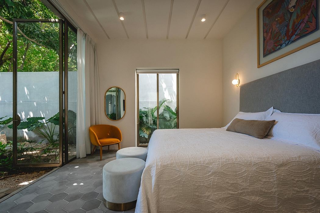 A bright, airy bedroom with a patterned bedspread, plush armchair, and floor-to-ceiling windows.