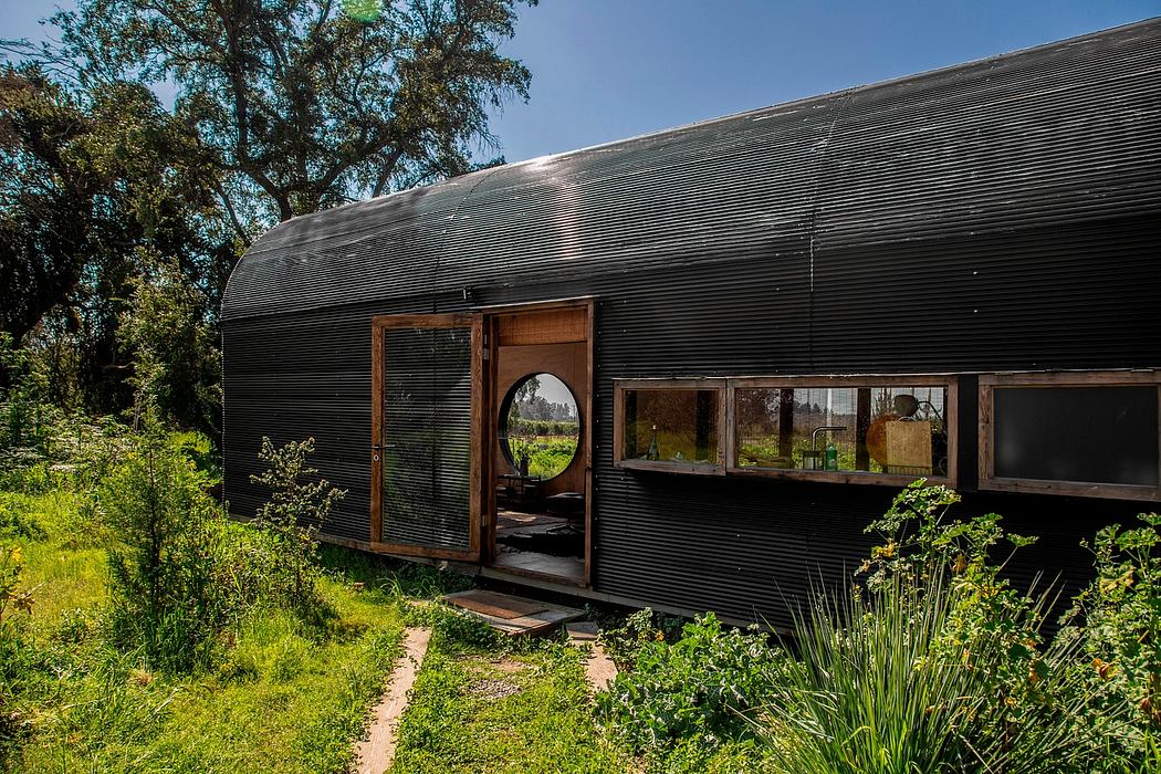 Rustic, curved corrugated metal exterior with large windows, set in a lush garden.