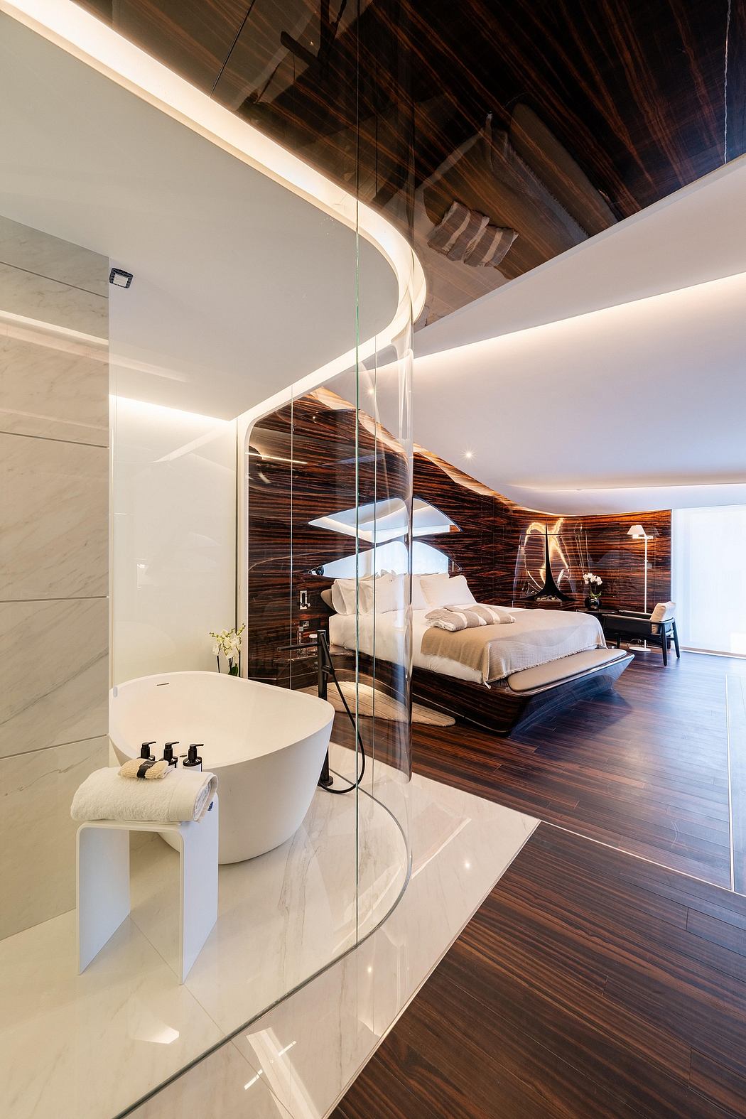 Luxurious, open-concept bedroom with curved glass walls, wooden accent walls, and a freestanding bathtub.