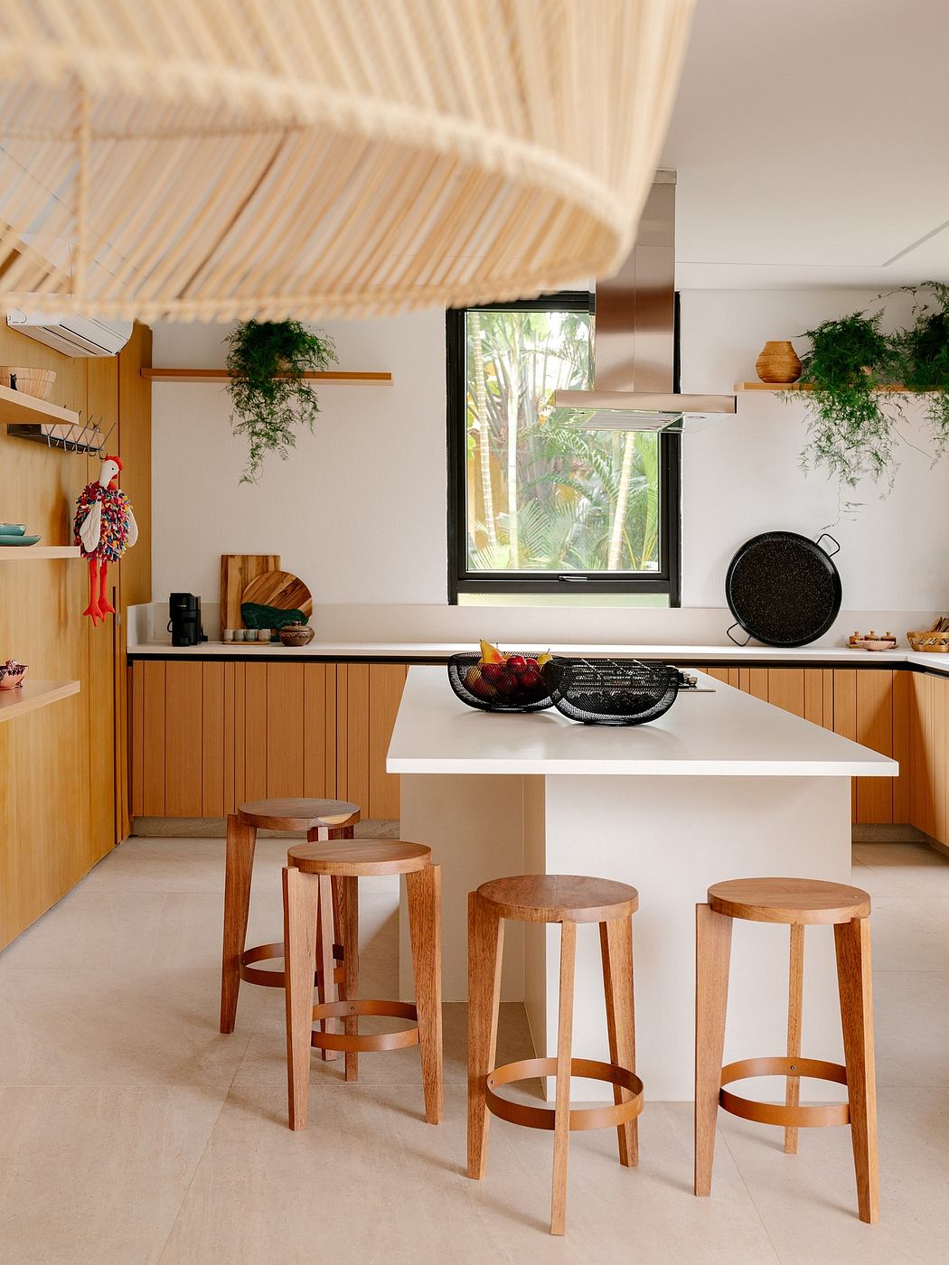 Spacious kitchen with wooden accents, hanging plants, and a minimalist island with bar stools.