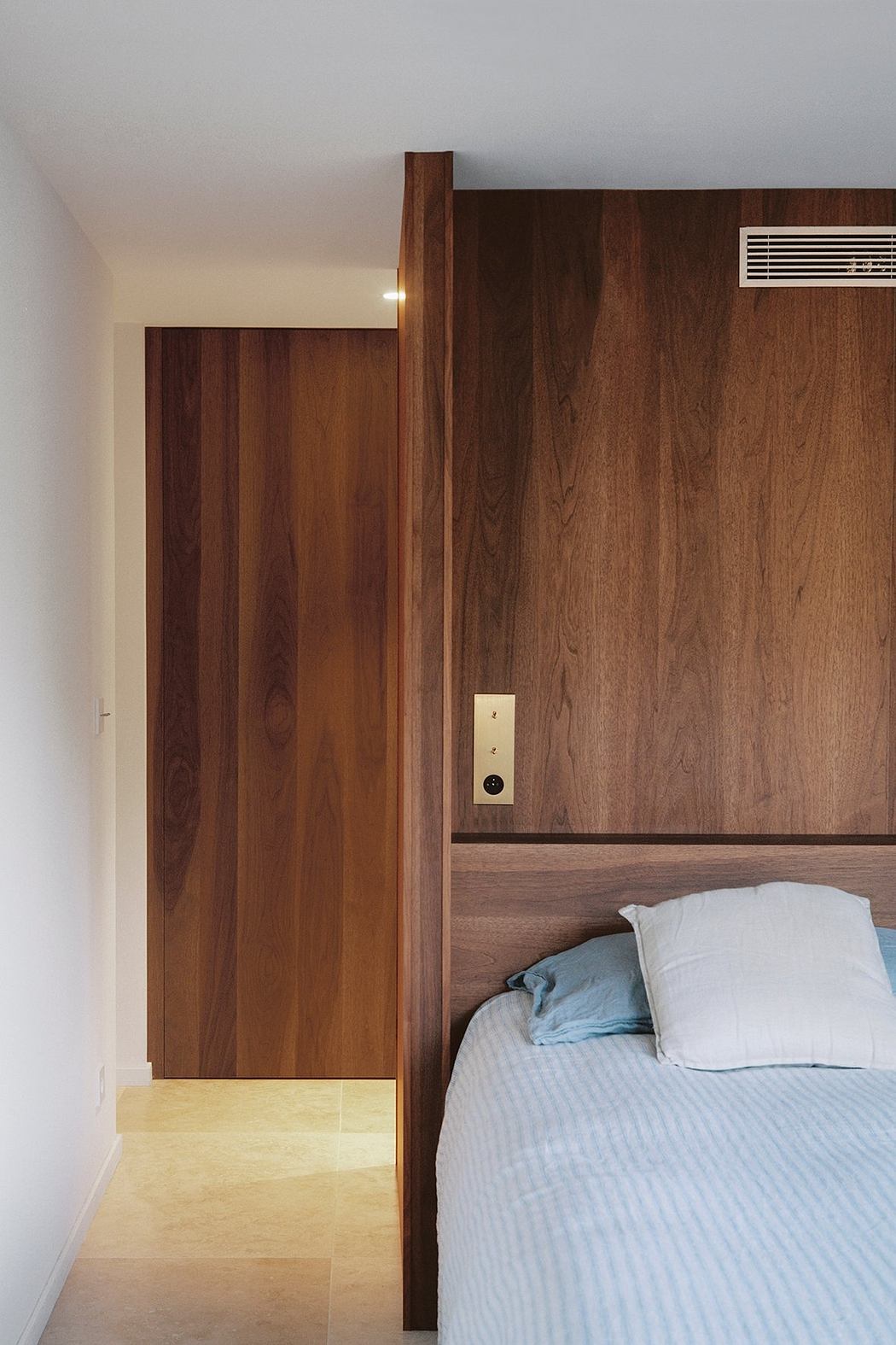 Minimalist bedroom design featuring wooden panels, recessed lighting, and a striped bedding.